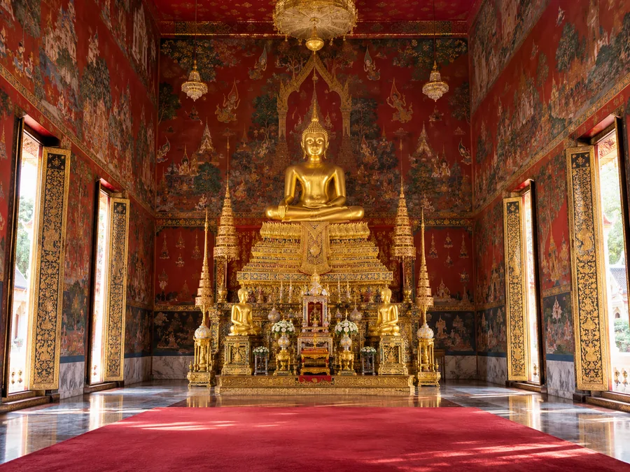 Eine goldene sitzende Buddhafigur auf einem vergoldeten Altar in einer Ordinationshalle mit bemalten Wandbildern
